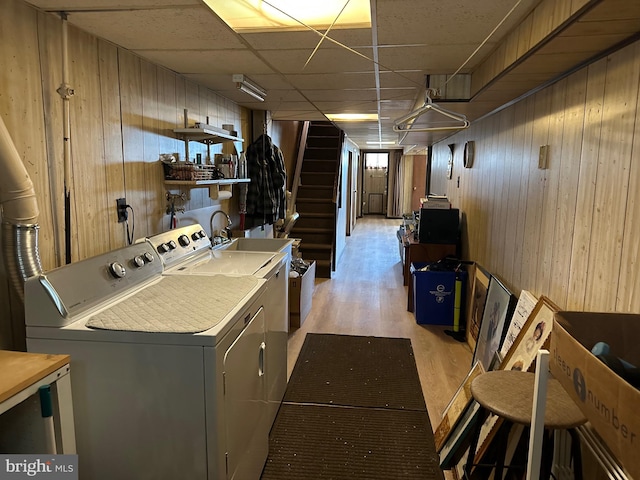 washroom featuring sink, wood walls, light hardwood / wood-style flooring, and washing machine and clothes dryer