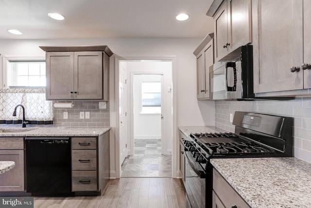 kitchen with light stone countertops, decorative backsplash, sink, and black appliances