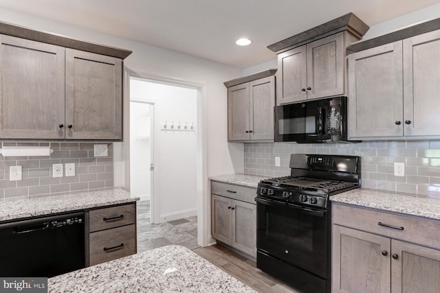 kitchen with tasteful backsplash, light stone counters, and black appliances