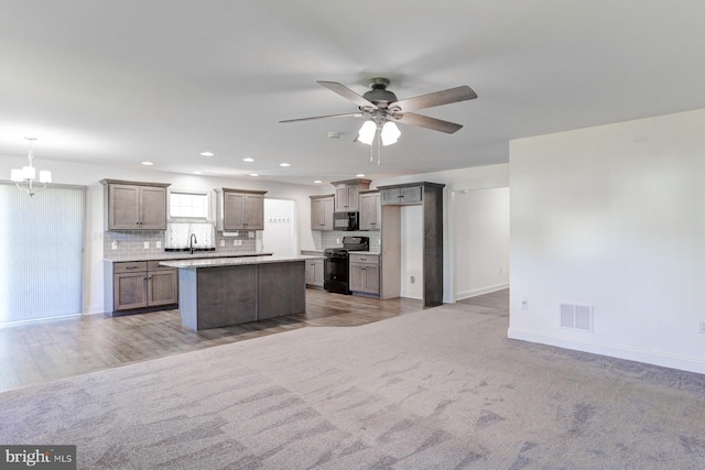 kitchen featuring sink, a kitchen island, decorative light fixtures, carpet, and black appliances