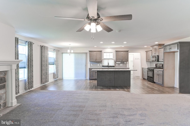 kitchen with backsplash, gas stove, sink, decorative light fixtures, and a center island