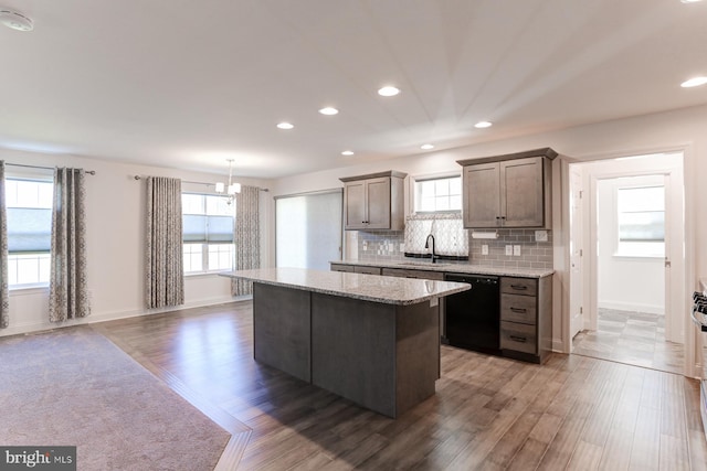 kitchen with a center island, hanging light fixtures, black dishwasher, light stone counters, and dark hardwood / wood-style floors