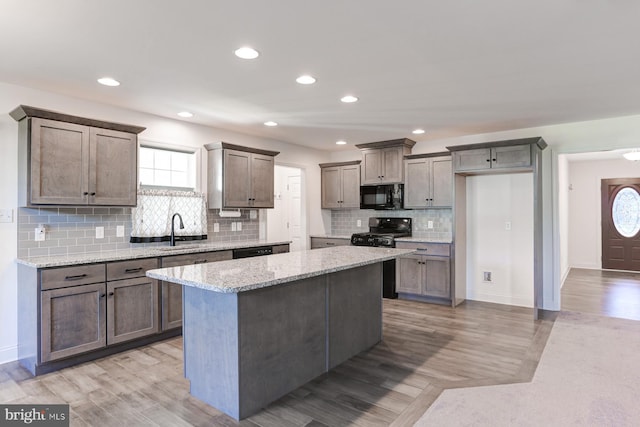 kitchen with a center island, black appliances, sink, light stone countertops, and a wealth of natural light