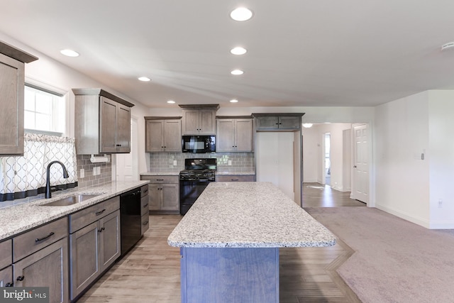 kitchen with light stone countertops, light colored carpet, sink, black appliances, and a center island