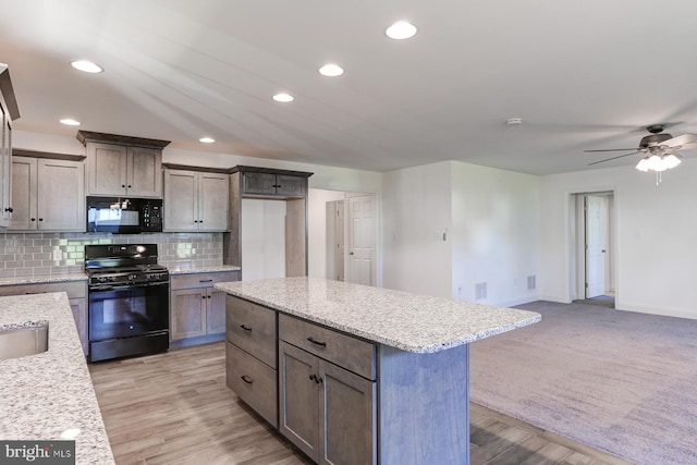 kitchen with light stone countertops, decorative backsplash, black appliances, light hardwood / wood-style flooring, and a kitchen island