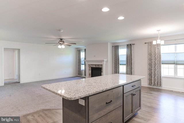 kitchen featuring ceiling fan with notable chandelier, a kitchen island, hanging light fixtures, and light stone counters