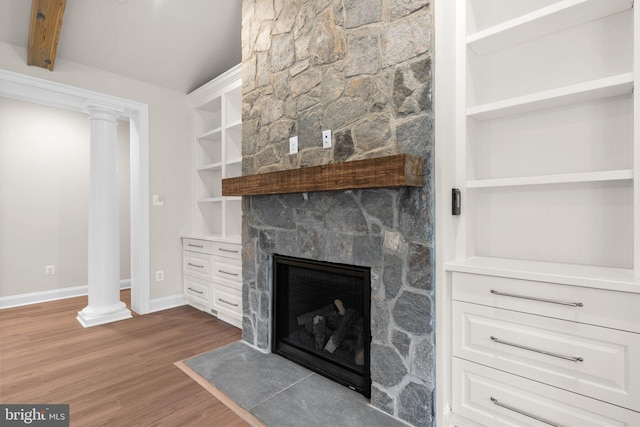 interior details with a stone fireplace, hardwood / wood-style floors, beam ceiling, and ornate columns