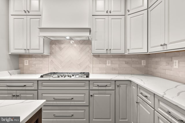 kitchen featuring stainless steel gas stovetop, light stone countertops, gray cabinetry, and tasteful backsplash