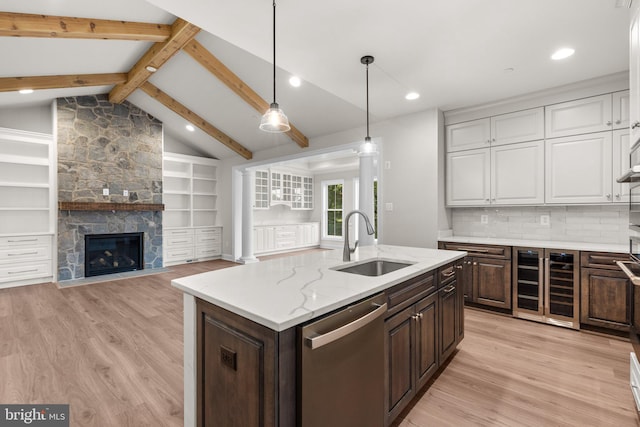 kitchen with sink, vaulted ceiling with beams, an island with sink, dark brown cabinets, and stainless steel dishwasher