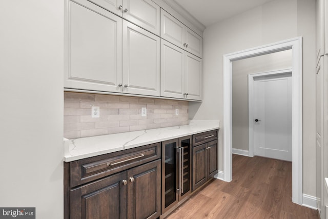 bar featuring white cabinets, beverage cooler, light stone countertops, light wood-type flooring, and dark brown cabinetry