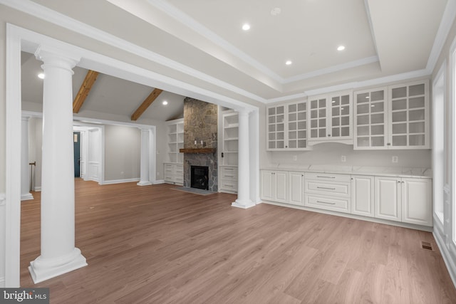 unfurnished living room with vaulted ceiling with beams, a stone fireplace, built in features, light hardwood / wood-style floors, and ornamental molding