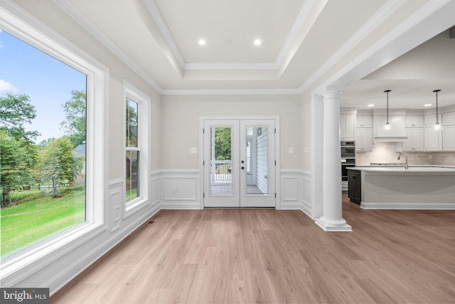 interior space featuring a raised ceiling, crown molding, ornate columns, light hardwood / wood-style floors, and french doors