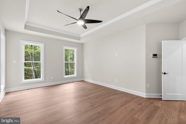 empty room with ceiling fan, a tray ceiling, and light wood-type flooring