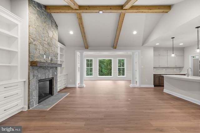 unfurnished living room featuring vaulted ceiling with beams, hardwood / wood-style flooring, a fireplace, and built in shelves