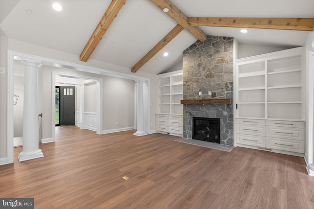 unfurnished living room featuring vaulted ceiling with beams, light hardwood / wood-style flooring, a stone fireplace, and decorative columns