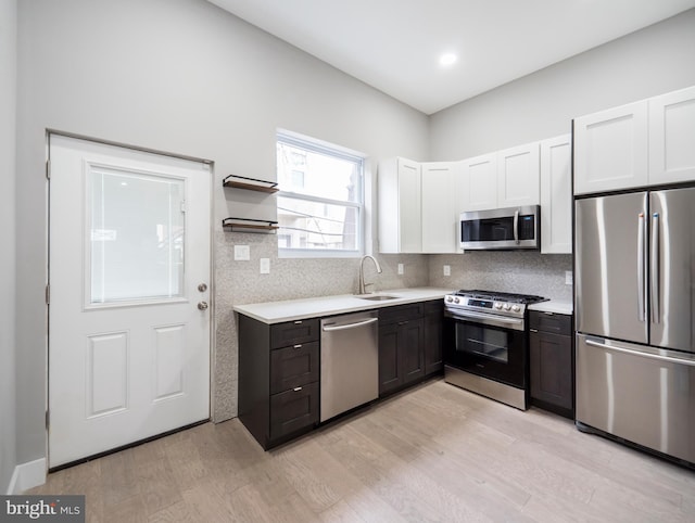 kitchen with stainless steel appliances, tasteful backsplash, sink, white cabinetry, and light hardwood / wood-style flooring