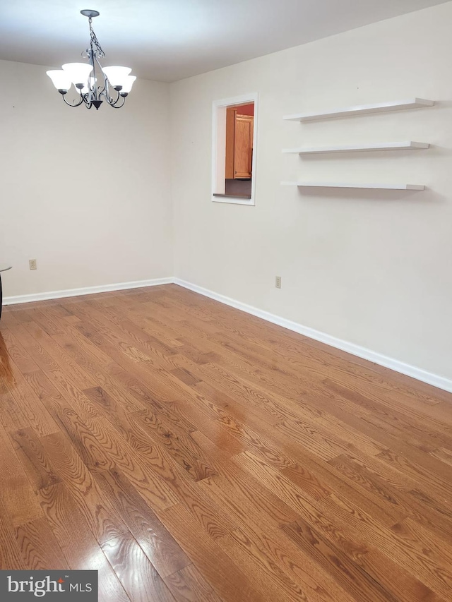 spare room with an inviting chandelier and hardwood / wood-style floors