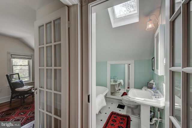 bathroom featuring french doors, tile patterned floors, a washtub, lofted ceiling with skylight, and toilet