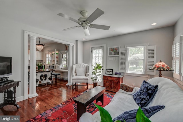 living room featuring ornate columns, dark wood-type flooring, and ceiling fan with notable chandelier