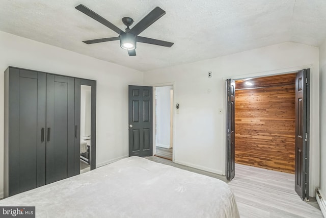 bedroom featuring baseboard heating, ceiling fan, light hardwood / wood-style floors, and a textured ceiling