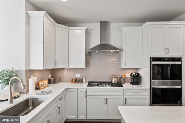 kitchen featuring white cabinets, wall chimney range hood, sink, and stainless steel appliances