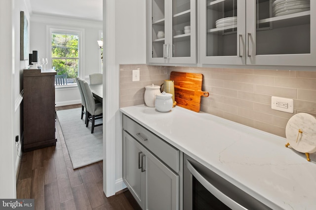 kitchen with light stone countertops, dark wood-type flooring, tasteful backsplash, crown molding, and gray cabinets