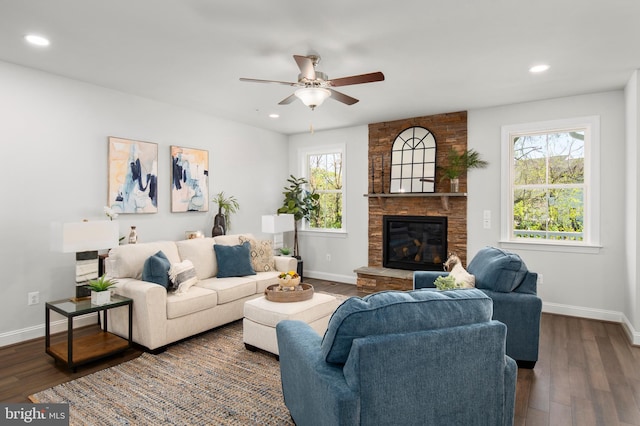 living room with a stone fireplace, ceiling fan, and dark wood-type flooring