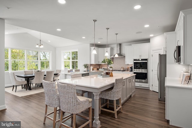 kitchen featuring white cabinets, appliances with stainless steel finishes, lofted ceiling, and wall chimney exhaust hood