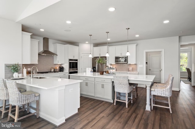 kitchen with a center island, white cabinets, wall chimney range hood, appliances with stainless steel finishes, and decorative light fixtures