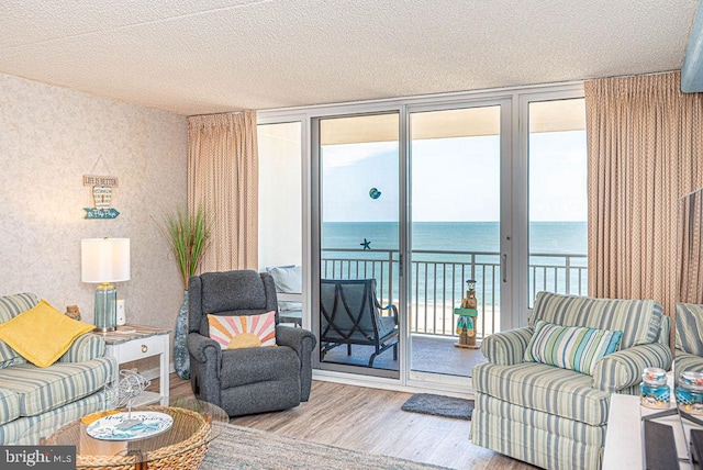 living room featuring a water view, light hardwood / wood-style floors, floor to ceiling windows, and a textured ceiling