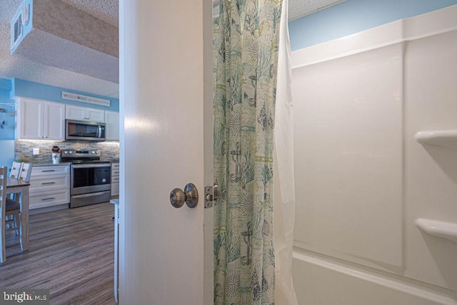 bathroom with shower / tub combo with curtain, backsplash, hardwood / wood-style floors, and a textured ceiling