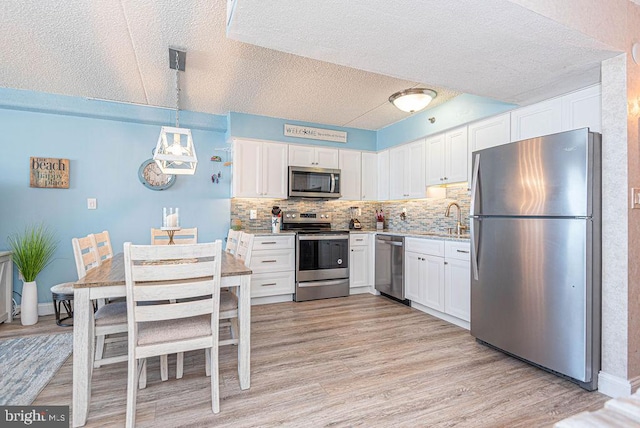 kitchen featuring stainless steel appliances, decorative light fixtures, light wood-type flooring, and white cabinetry