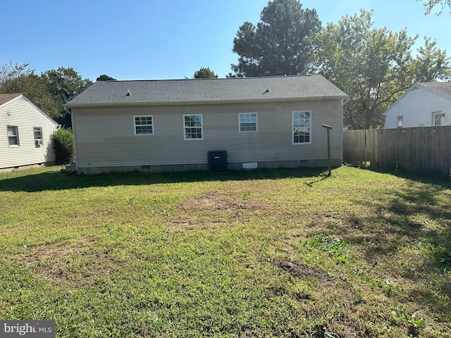 rear view of house with central air condition unit and a lawn