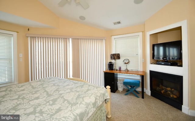 carpeted bedroom featuring a glass covered fireplace, vaulted ceiling, visible vents, and ceiling fan