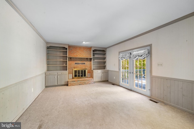 unfurnished living room featuring french doors, light carpet, a fireplace, built in features, and ornamental molding