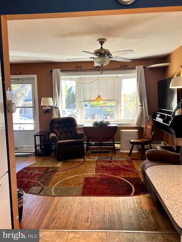 living room with baseboard heating, hardwood / wood-style floors, and ceiling fan