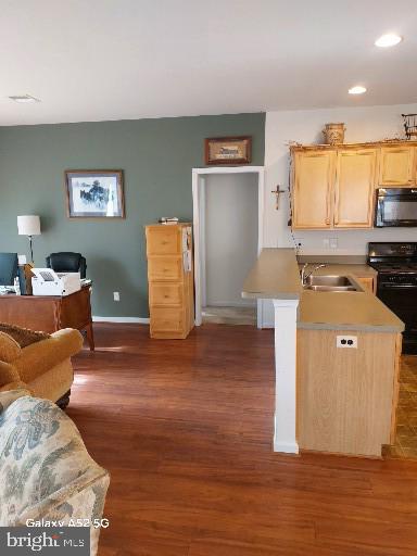 kitchen with black range with electric cooktop, a center island with sink, light brown cabinetry, sink, and dark wood-type flooring