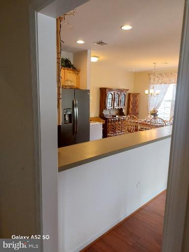 kitchen featuring decorative light fixtures, black fridge with ice dispenser, an inviting chandelier, hardwood / wood-style flooring, and kitchen peninsula