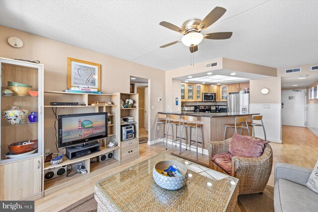 living room with light hardwood / wood-style flooring, a textured ceiling, and ceiling fan