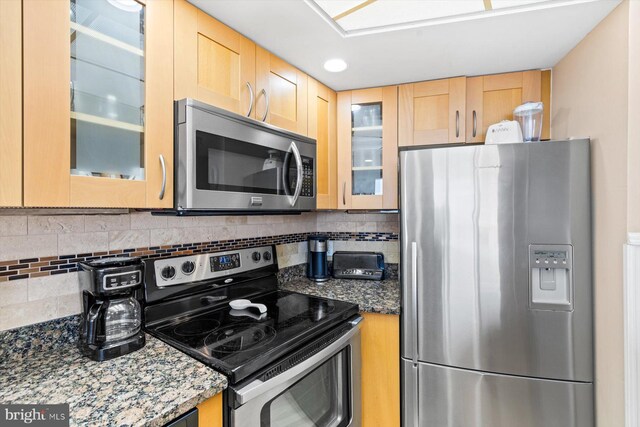 kitchen featuring light brown cabinetry, tasteful backsplash, appliances with stainless steel finishes, and dark stone counters