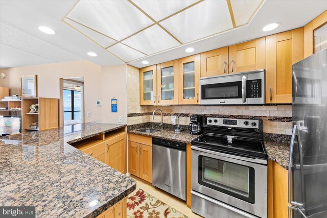 kitchen featuring kitchen peninsula, dark stone countertops, stainless steel appliances, and sink