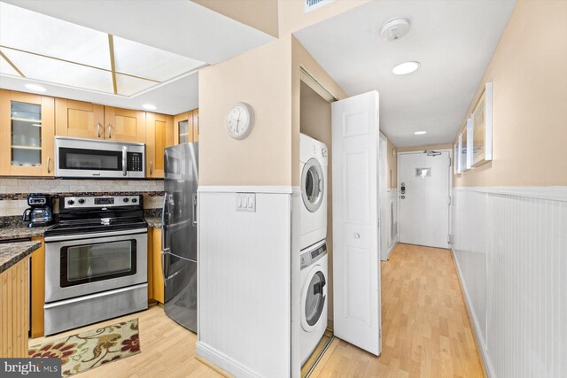 kitchen with stacked washing maching and dryer, tasteful backsplash, appliances with stainless steel finishes, and light hardwood / wood-style floors