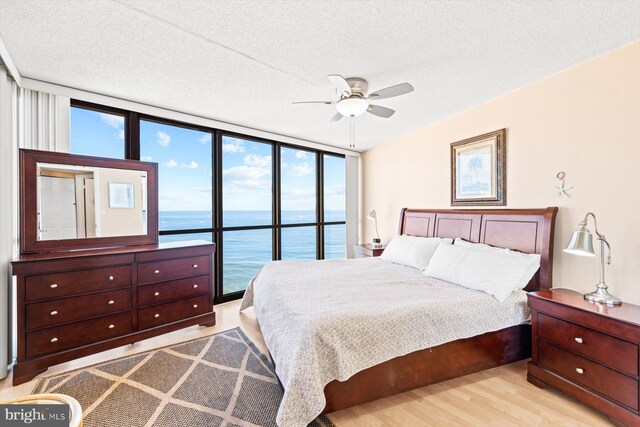 bedroom featuring floor to ceiling windows, a water view, light wood-type flooring, and ceiling fan