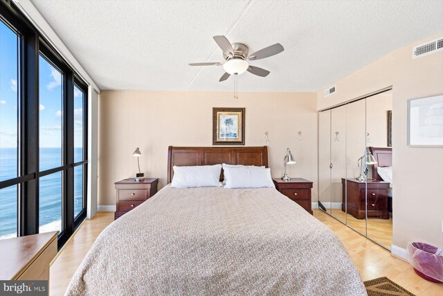 bedroom with a closet, a water view, a textured ceiling, light hardwood / wood-style floors, and ceiling fan