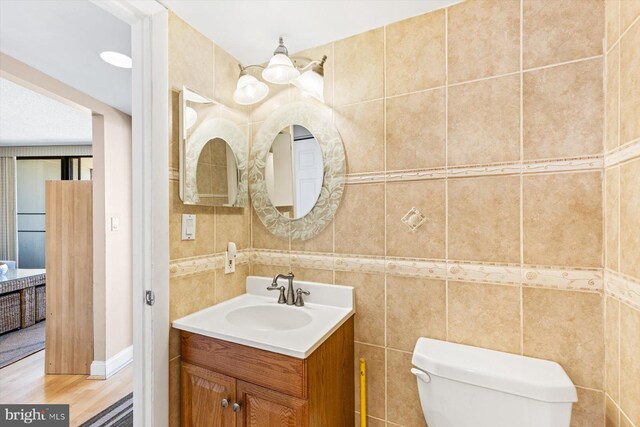 bathroom with toilet, hardwood / wood-style flooring, vanity, and tile walls