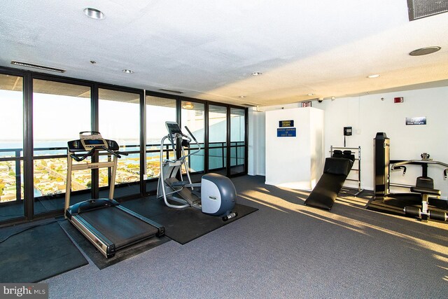 exercise room featuring a textured ceiling, a water view, and floor to ceiling windows