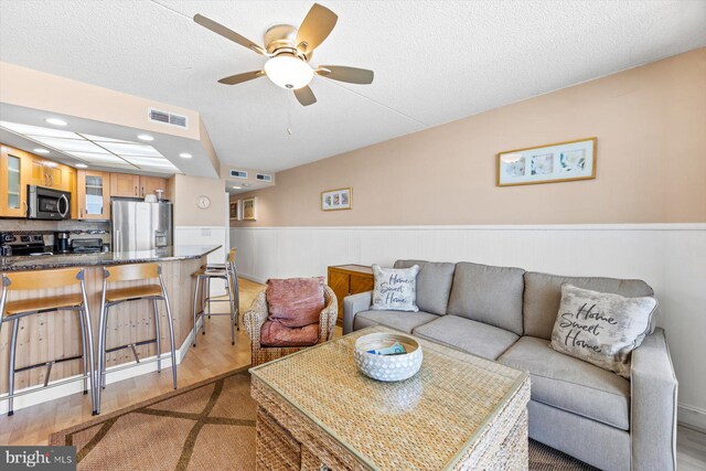 living room with light hardwood / wood-style flooring, a textured ceiling, and ceiling fan