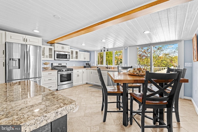 kitchen featuring white cabinetry, stainless steel appliances, glass insert cabinets, and stone tile floors