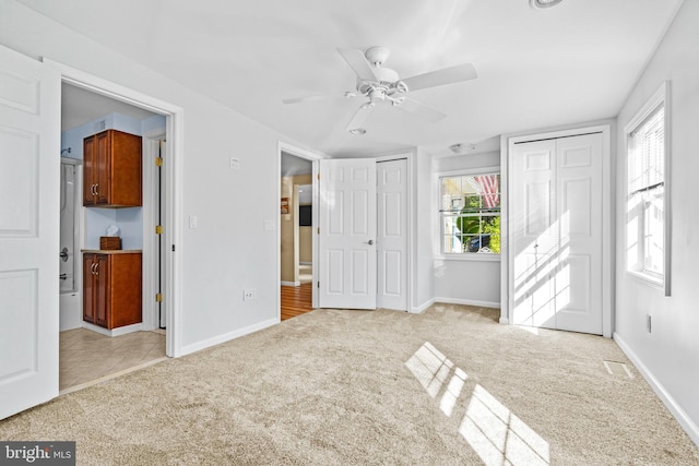 unfurnished bedroom with two closets, ensuite bath, a ceiling fan, baseboards, and light colored carpet