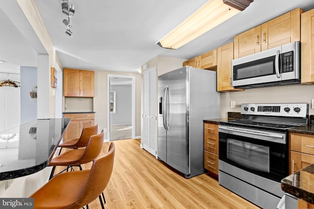 kitchen with a breakfast bar area, light wood-type flooring, stainless steel appliances, and dark stone countertops
